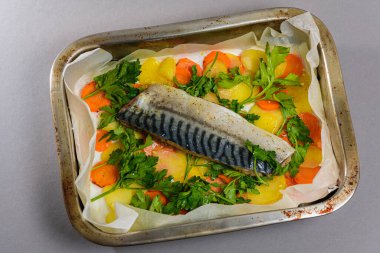 Fırında pişirmeden önce sebzeli, patatesli, havuçlu taze moraine uskumrusu, metal bir şekilde. Sebzeli balık. Gri arkaplan, üst manzara. Ev yemekleri..