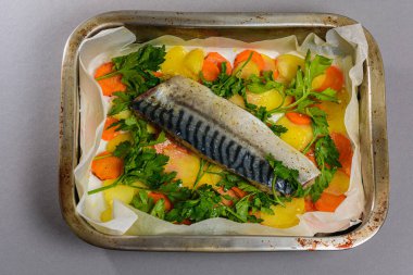 Fırında pişirmeden önce sebzeli, patatesli, havuçlu taze moraine uskumrusu, metal bir şekilde. Sebzeli balık. Gri arkaplan, üst manzara. Ev yemekleri..