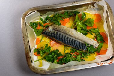 Fırında pişirmeden önce sebzeli, patatesli, havuçlu taze moraine uskumrusu, metal bir şekilde. Sebzeli balık. Gri arkaplan, üst manzara. Ev yemekleri..