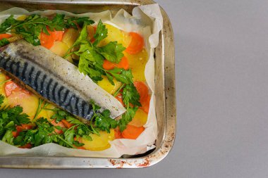 Fırında pişirmeden önce sebzeli, patatesli, havuçlu taze moraine uskumrusu, metal bir şekilde. Sebzeli balık. Gri arkaplan, üst manzara. Ev yemekleri..