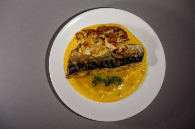 Soslu fırında uskumru balığı, karnabahar ve beyaz bir tabakta sarı püre. Sebzeyle pişirilmiş balık. Gri arka plan. Üst görünüm.