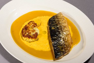 Soslu fırında uskumru balığı, karnabahar ve beyaz bir tabakta sarı püre. Sebzeyle pişirilmiş balık. Gri arka plan. Üst görünüm.