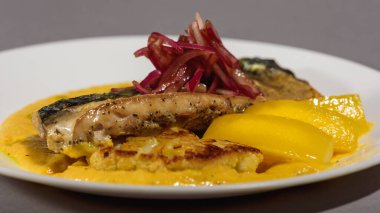 Sos ve soğanlı fırında uskumru balığı ve beyaz bir tabakta sarı püre. Sebzeyle pişirilmiş balık. Gri arka plan. Üst görünüm