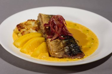 Sos ve soğanlı fırında uskumru balığı ve beyaz bir tabakta sarı püre. Sebzeyle pişirilmiş balık. Gri arka plan. Üst görünüm.