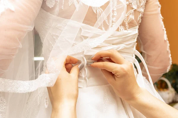 新婦付添人は結婚式の日のための花嫁を準備し ボタンを助け 彼女の服を結ぶ 新婦付添人が花嫁の結婚式のドレスの後ろに弓を作る花嫁の朝の集会 — ストック写真