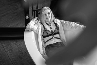 Genç, seksi, oldukça rahat gülümseyen bir kadın lüks bir banyoda uzanıyor, eğleniyor, yeşil bitkiler, İskandinav iç tasarımı, çizgili deri elbiseler. Seçici odaklanma. Siyah ve beyaz