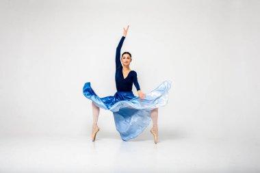 Güzel balerin dansı, açık arkaplanda uzun mavi bir elbiseyle kameraya doğru bakan çeşitli egzersizler gösterir. Seçici odaklanma, hareket