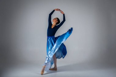 Genç, güzel balerin açık arka planda uzun mavi bir elbiseyle dans ediyor. Bale, dans, dansçı.