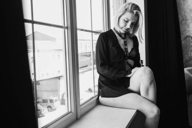 Portrait of a black and white young, pretty European girl emotional in a men's shirt in the bedroom near a large window, smiles, straightens hair. Morning sun, selective focus 