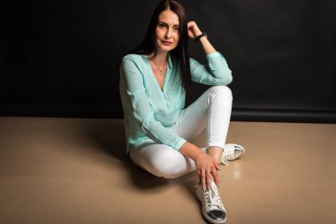 Portrait, studio shot of smiling pretty attractive attractive young middle-aged girl sitting on the floor smiling, on dark background. Place for post 