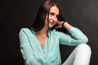 Portrait, studio shot of smiling pretty attractive attractive young middle-aged girl sitting on the floor smiling, on dark background. Place for post 