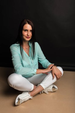 Portrait, studio shot of smiling pretty attractive attractive young middle-aged girl sitting on the floor smiling, on dark background. Place for post 