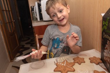 Yan görünüş, renkli Paskalya el yapımı eşyalar, fırın, masada uzanan kurabiyeler ve boyanmış küçük kurabiyeler. Çocuk anne için zencefilli ekmek boyuyor. Anneler Günün kutlu olsun.