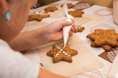 Üst manzara, renkli Paskalya objeleri, fırın, masada ve ellerde duran kurabiyeler boyalı, küçük, süslü kurabiyeler. Çocuklar anneler için zencefilli kurabiye süslüyor. Mutlu anneler günleri.