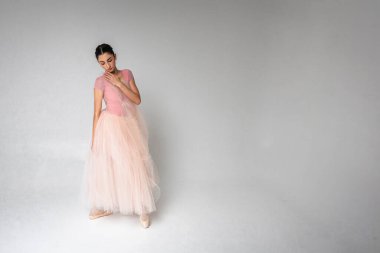 Genç, güzel, narin, güzel balerin. Uzun soluk pembe bir elbiseyle dans ediyor. Üniformalı bir arka planı var. Bale, dans, dansçı.