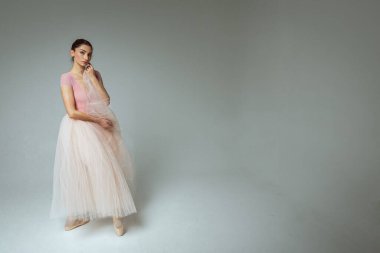 Genç, güzel, narin, güzel balerin. Uzun soluk pembe bir elbiseyle dans ediyor. Üniformalı bir arka planı var. Bale, dans, dansçı.