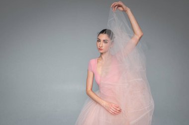 Genç, güzel, narin, güzel balerin. Uzun soluk pembe bir elbiseyle dans ediyor. Üniformalı bir arka planı var. Bale, dans, dansçı.