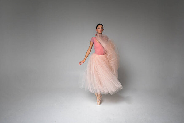молодая красивая, хрупкая, красивая балерина танцует в длинном бледно-розовом платье с тюлем на однородном фоне, сдержанный. Балет, танцы, танцоры
