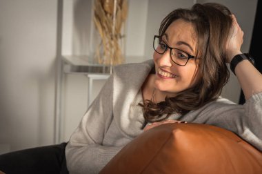 Başarı konsepti. Şık, genç, duygusal, gözlüklü, işyerindeki deri koltukta oturan, gülümseyen