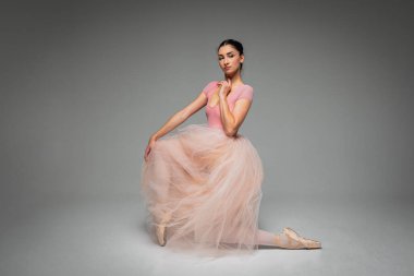 Genç, güzel, narin, güzel balerin. Uzun soluk pembe bir elbiseyle dans ediyor. Üniformalı bir arka planı var. Bale, dans, dansçı. Yazı için yer