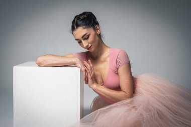 Balerin yorgundu ve beyaz meydanda oturdu. Genç, güzel, kırılgan, güzel balerin, uzun açık pembe bir elbise içinde, arka planda tülleri olan, kısıtlı bir tonda oturdu. Bale, dans