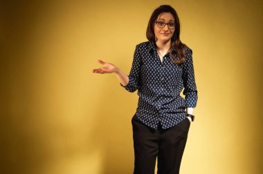 Koyu renk pantolonlu, gömlekli, duygusal, gülümseyen bir kadın. Örgü gömlekli çekici kız sarı arka planda dans ediyor. Genç bir kızın portresi. Yazı için yer