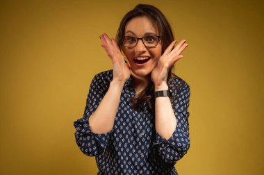 Genç, duygusal, güzel, şaşkın, koyu renk pantolonlu ve gömlekli, el hareketleri gösteren, sarı arka planda izole edilmiş bir bayan. Genç bir kızın portresi. Yazı için yer