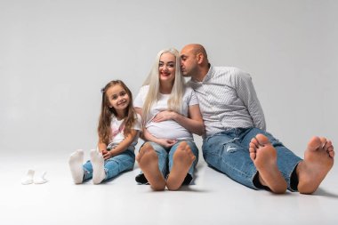 Üç kişilik mutlu bir aile yerde oturuyor. Anne, baba ve küçük çocuk. Annem hamile. Haberler iyi, hamile, ayaklarımız çıplak.