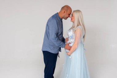 Yakışıklı, duygusal bir adam ve güzel hamile kadının homojen bir arka planda sarılıp gülümsemesi. Bir aile kurmak, çocuk sahibi olmak.