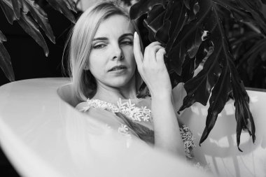 Black and white classic photo. Woman relaxes in a round open bath with tropical flowers, organic skin care, luxury spa hotel, lifestyle photos. Selective focus
