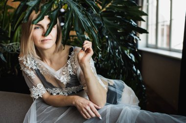 Genç, güzel bir kız, pencerenin kenarında tropikal çiçekler, yeşil yapraklar, kanepeye yaslanmış, organik cilt bakımı, lüks spa oteli, yaşam tarzı fotoğrafları..