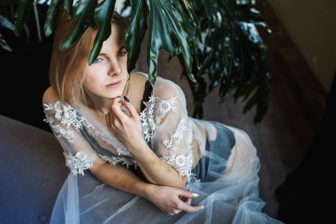 Genç, güzel bir kız, pencerenin kenarında tropikal çiçekler, yeşil yapraklar, kanepeye yaslanmış, organik cilt bakımı, lüks spa oteli, yaşam tarzı fotoğrafları..