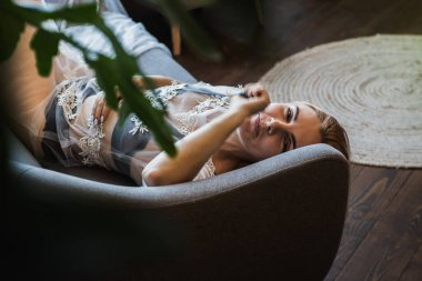 Genç, güzel, duygusal sarışın kız yatakta yatıyor, manzarası güzel, manzarası güzel, yeşil yaprakların arasından bakıyor. Seçici odaklanma. Rahatla ve dinlen.