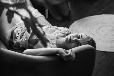 Siyah beyaz klasik fotoğraf, siyah bir yatakta uzanan deri kayışlı seksi iç çamaşırlı güzel manken. Kız ve iç çamaşırı kavramı.