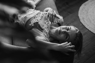 Siyah beyaz klasik fotoğraf, siyah bir yatakta uzanan deri kayışlı seksi iç çamaşırlı güzel manken. Kız ve iç çamaşırı kavramı.