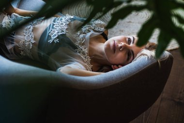 Genç, güzel, duygusal sarışın kız yatakta yatıyor, manzarası güzel, manzarası güzel, yeşil yaprakların arasından bakıyor. Seçici odaklanma. Rahatla ve dinlen.