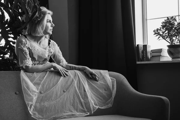 Genç, güzel bir kız, pencerenin yanında tropik çiçekleri, yeşil yaprakları, kanepeye yaslanmış, organik cilt bakımı, lüks spa oteli. Siyah beyaz klasik fotoğraf. Seçici odak