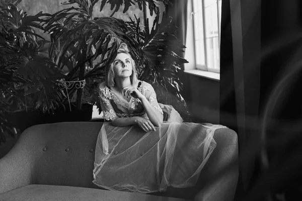 Genç, güzel bir kız, pencerenin yanında tropik çiçekleri, yeşil yaprakları, kanepeye yaslanmış, organik cilt bakımı, lüks spa oteli. Siyah beyaz klasik fotoğraf. Seçici odak