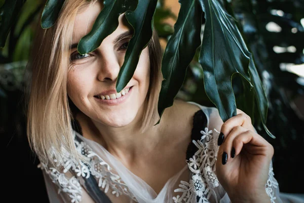 Genç, güzel bir kız, pencerenin kenarında tropikal çiçekler, yeşil yapraklar, kanepeye yaslanmış, organik cilt bakımı, lüks spa oteli, yaşam tarzı fotoğrafları..