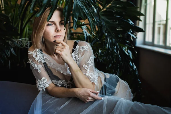 Genç, güzel bir kız, pencerenin kenarında tropikal çiçekler, yeşil yapraklar, kanepeye yaslanmış, organik cilt bakımı, lüks spa oteli, yaşam tarzı fotoğrafları..