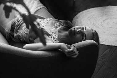 Siyah beyaz klasik fotoğraf, siyah bir yatakta uzanan deri kayışlı seksi iç çamaşırlı güzel manken. Kız ve iç çamaşırı kavramı.