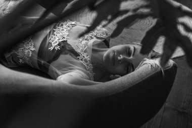 Siyah beyaz klasik fotoğraf, siyah bir yatakta uzanan deri kayışlı seksi iç çamaşırlı güzel manken. Kız ve iç çamaşırı kavramı.