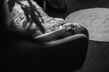 Siyah beyaz klasik fotoğraf, siyah bir yatakta uzanan deri kayışlı seksi iç çamaşırlı güzel manken. Kız ve iç çamaşırı kavramı.