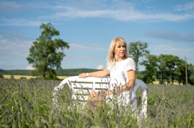 Genç bir kız sonsuz lavanta tarlasının ortasında bir bankta oturuyor. Gündüz çekilmiş bir portre resmi.