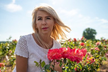 young pretty fair-haired girl near a rose bush looks to the side, nature, travel, rest