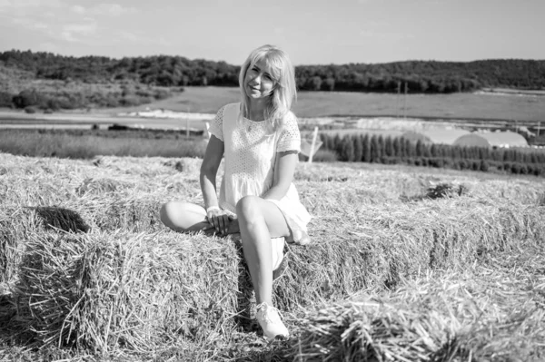 young fair-haired girl sitting on hay, freshly cut haystacks, straw, looking to the side, black and white photo