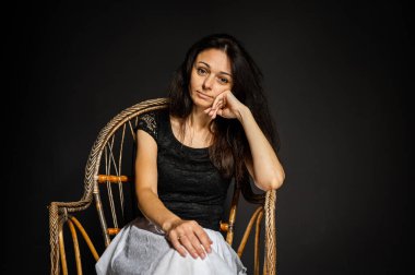 Heyecanlı, eğlenceli, çılgın, harika duygusal güzellik, ahşap sandalyede oturan genç kız karanlık arka planda harika bir ruh hali içinde.