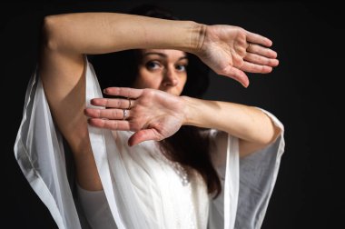 Endişe, tehlike, koruma. Bir kadının yüzünü elleriyle örttüğü kavramsal görüntü. Gözleriyle karanlık bir stüdyo arka planında parmaklarının arasından bakıyor.