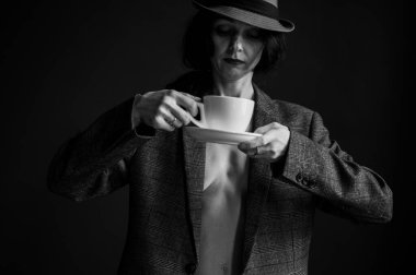 Şapkalı ve gri ceketli bir kız elinde sabah kahvesi ya da gri arka planda çay olan beyaz bir bardak tutuyor. Seçici odak, arkaplanda izole