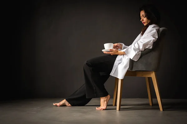 若いかなり 感情的な女の子は モダンな椅子に座って 灰色の背景にコーヒー サイドビュー 思慮深い 思考を楽しんでいます 書くための空間 — ストック写真